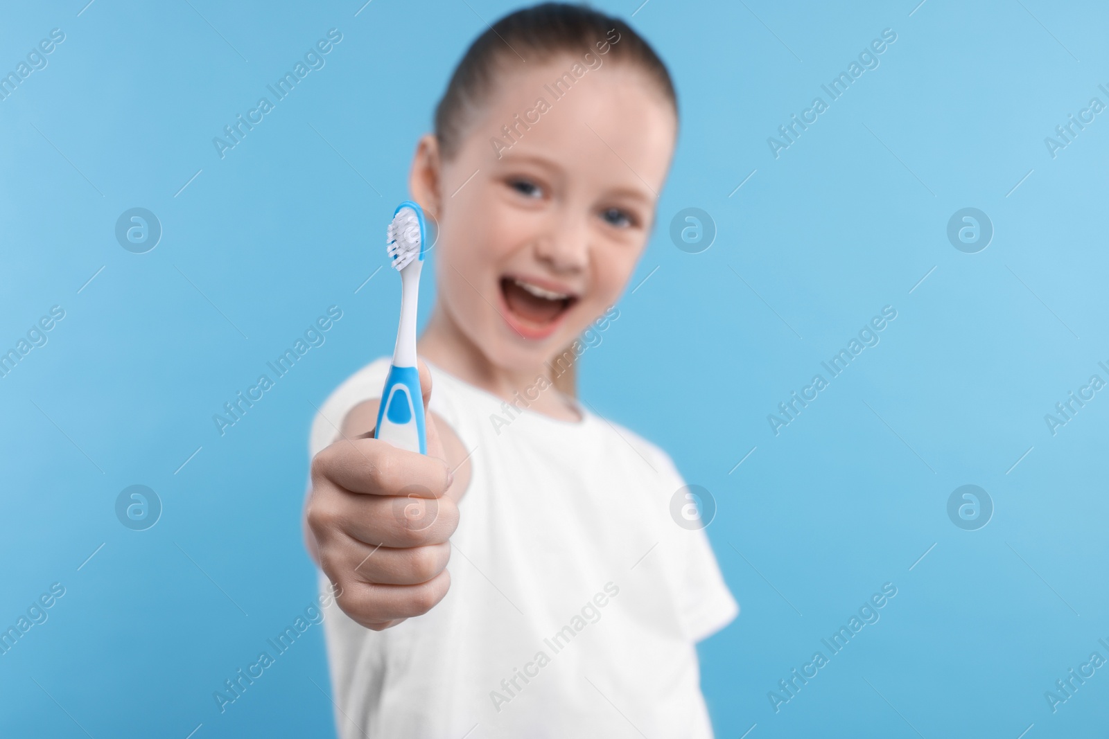 Photo of Happy girl holding toothbrush on light blue background, selective focus
