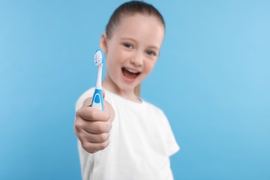 Happy girl holding toothbrush on light blue background, selective focus