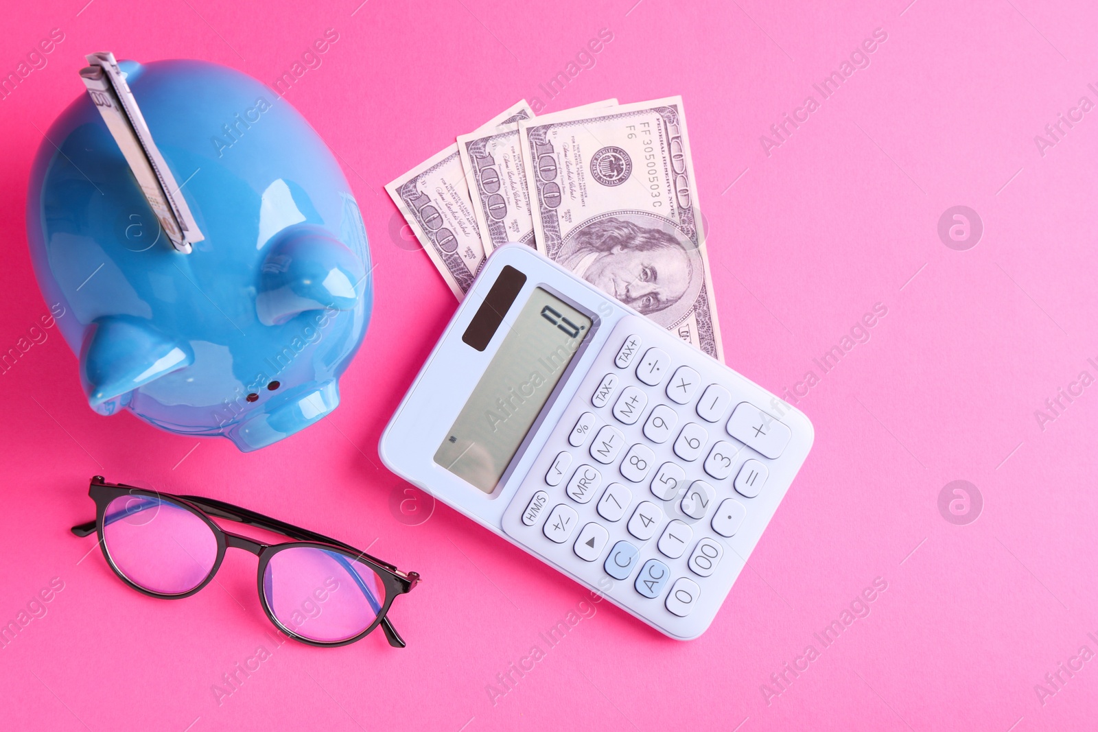 Photo of Financial savings. Piggy bank, dollar banknotes, glasses and calculator on pink background, flat lay