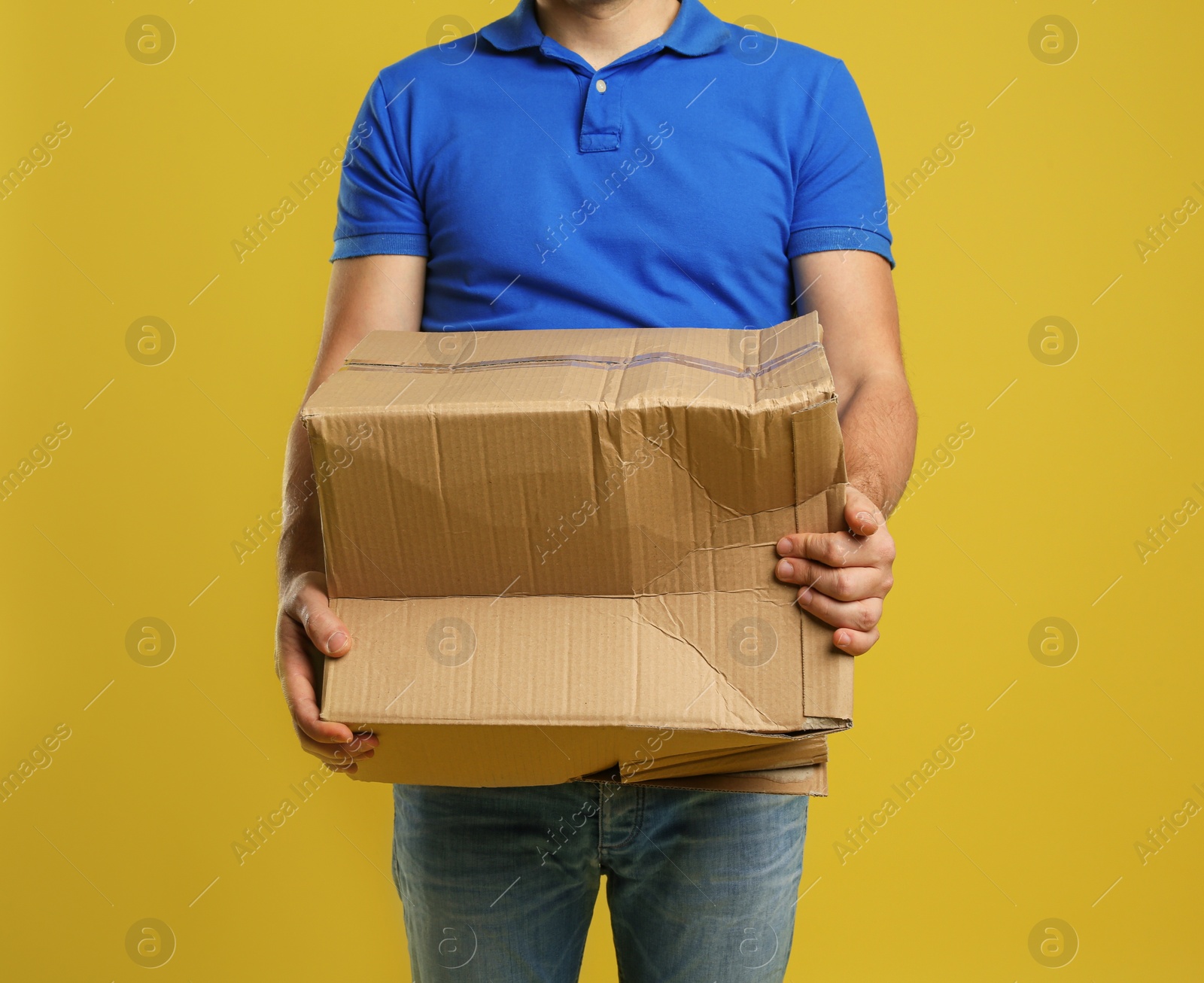Photo of Courier with damaged cardboard box on yellow background, closeup. Poor quality delivery service