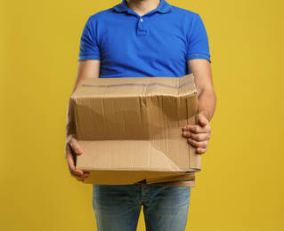 Photo of Courier with damaged cardboard box on yellow background, closeup. Poor quality delivery service
