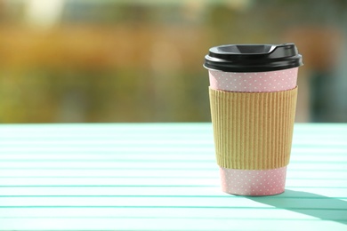 Photo of Cardboard cup of coffee on table against blurred background. Space for text