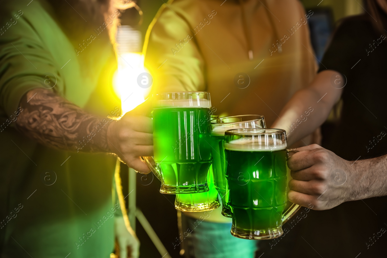 Photo of Group of friends toasting with green beer in pub, closeup. St. Patrick's Day celebration