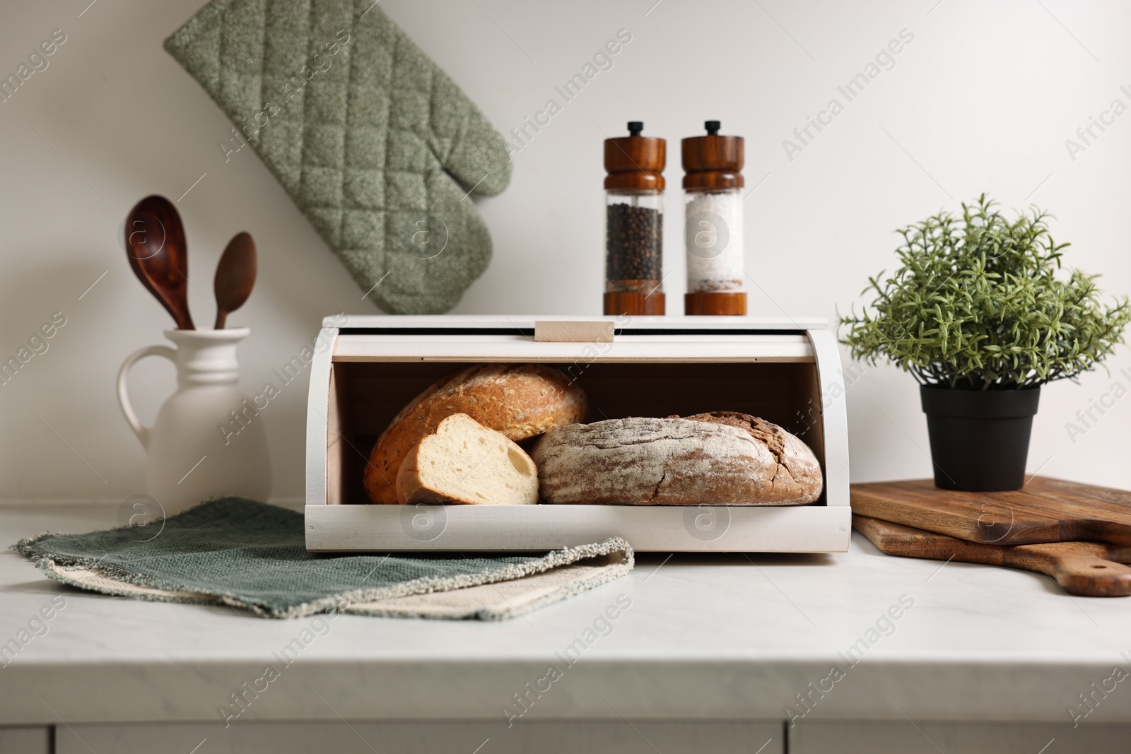 Photo of Wooden bread basket with freshly baked loaves on white marble table in kitchen