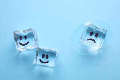 Photo of Ice cubes with drawn faces on light blue background, flat lay. Concept of jealousy