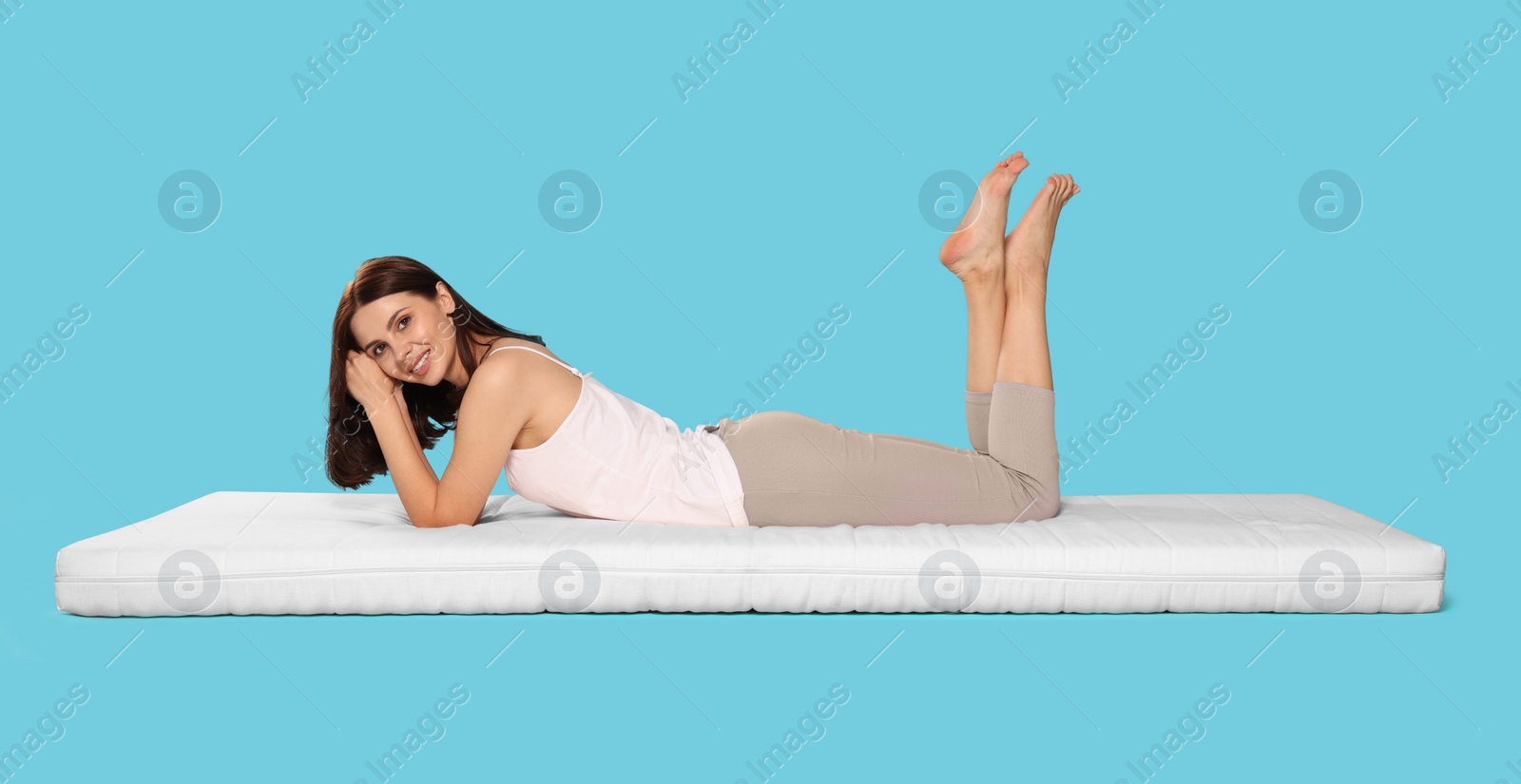 Photo of Young woman lying on soft mattress against light blue background