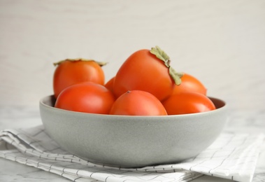 Tasty ripe persimmons in bowl on table, closeup