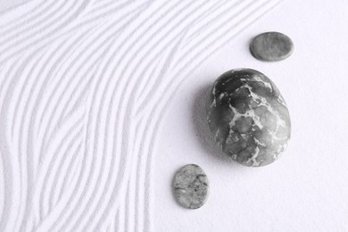 Photo of Zen garden stones on white sand with pattern, flat lay