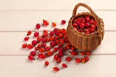 Ripe rose hip berries with wicker basket on white wooden table, above view