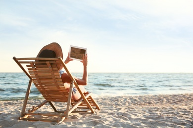 Photo of Young woman with tablet relaxing in deck chair on beach