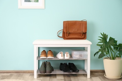 Photo of Collection of stylish shoes on rack storage near color wall in room