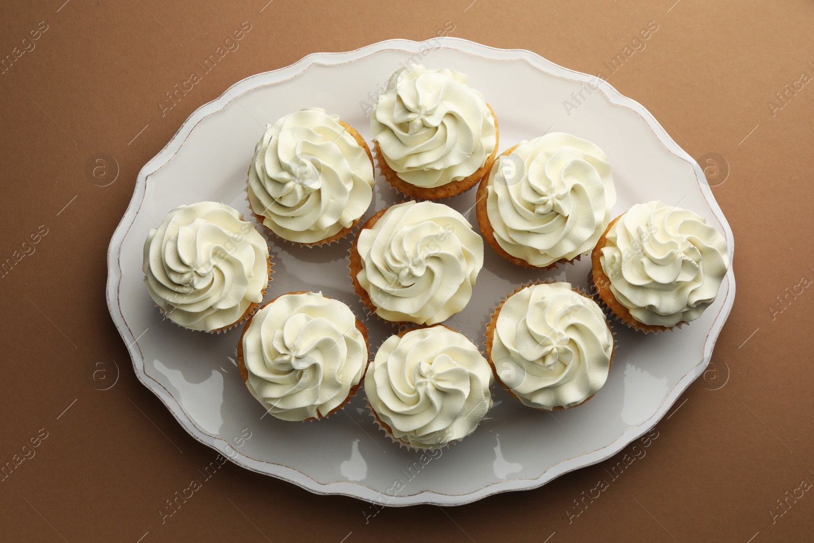 Photo of Tasty vanilla cupcakes with cream on dark beige background, top view