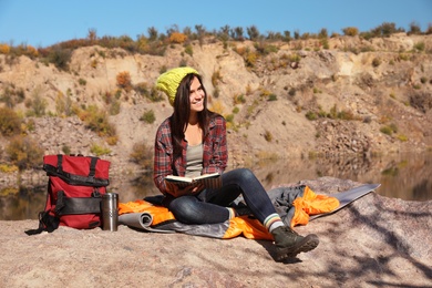 Female camper reading book while sitting on sleeping bag in wilderness