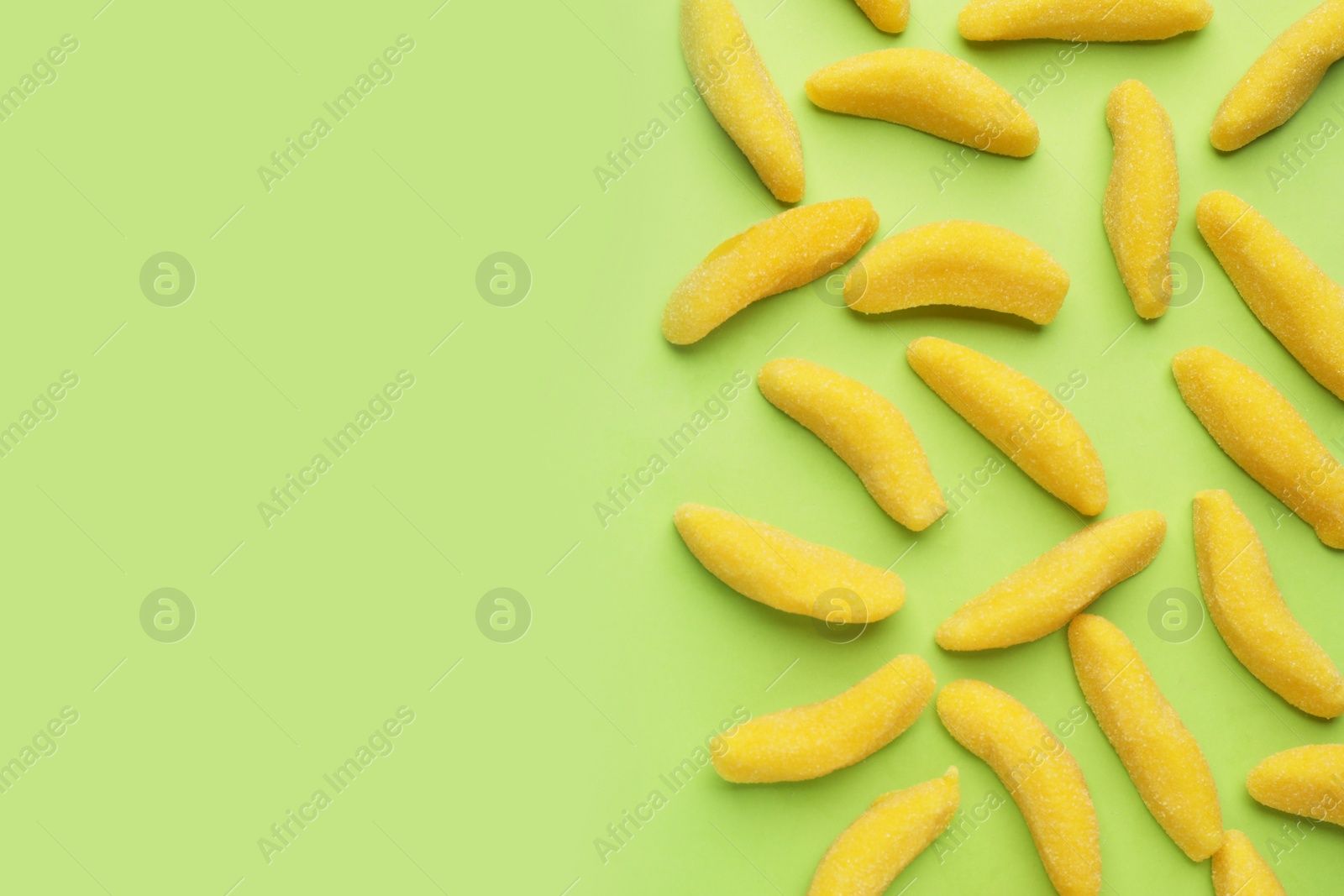 Photo of Tasty jelly candies in shape of banana on green background, flat lay. Space for text