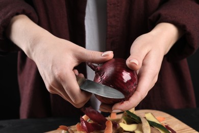 Woman peeling fresh onion with knife at table, closeup