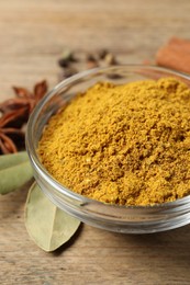 Curry powder in bowl and other spices on wooden table, closeup