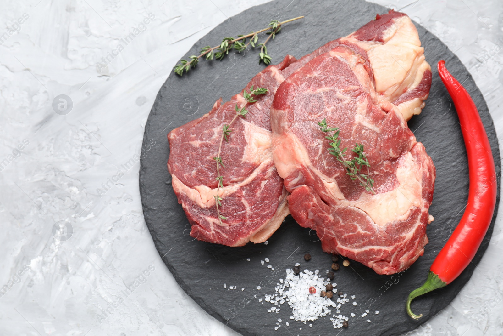 Photo of Fresh raw beef cut with different spices on light grey textured table, top view. Space for text