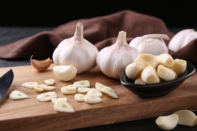 Aromatic cut garlic, cloves and bulbs on dark table, closeup