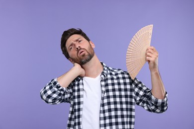 Photo of Unhappy man with hand fan suffering from heat on purple background