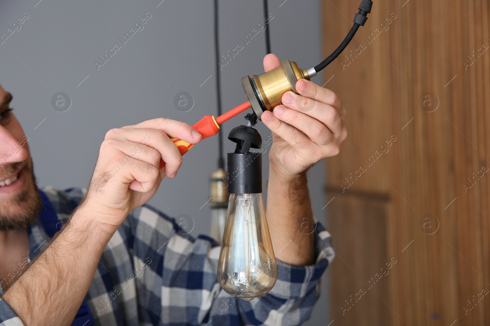 Photo of Electrician with screwdriver repairing ceiling lamp indoors, closeup