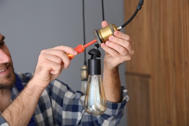 Electrician with screwdriver repairing ceiling lamp indoors, closeup