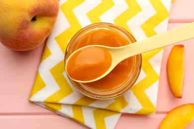 Photo of Spoon with healthy baby food over glass jar and fresh peaches on pink wooden table, flat lay