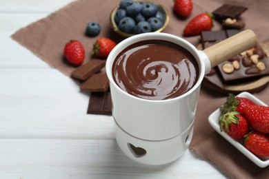 Photo of Fondue pot with chocolate and different berries on white wooden table, space for text