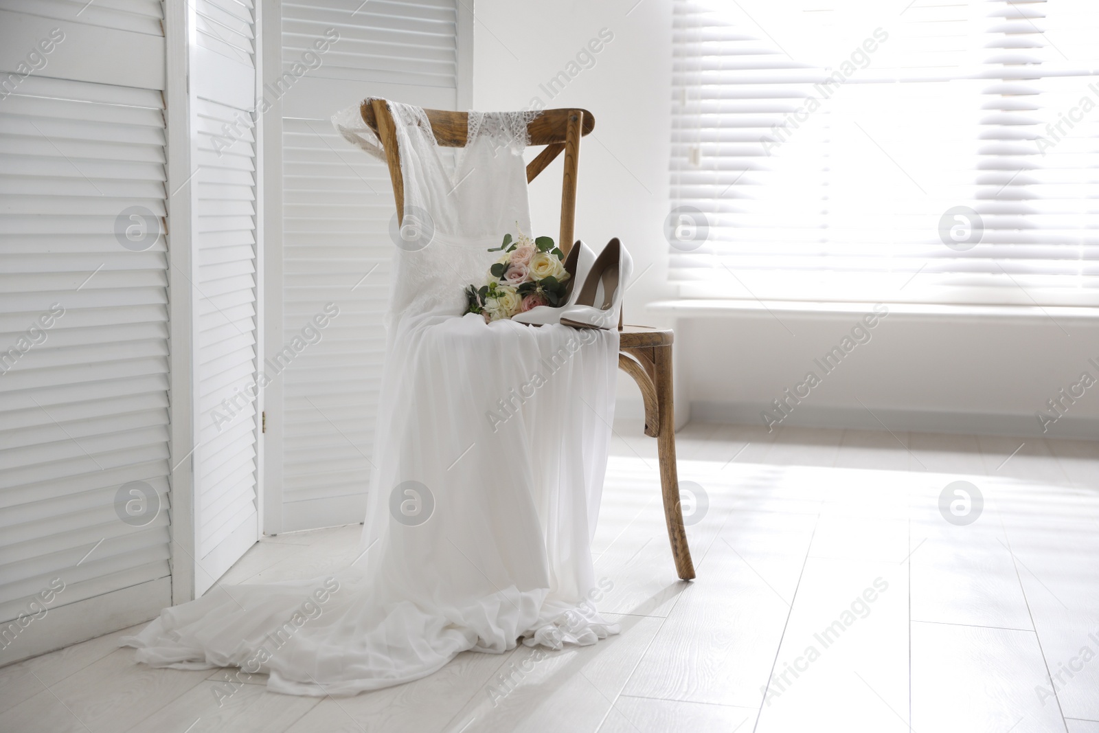 Photo of White high heel shoes, flowers and wedding dress on wooden chair indoors. Space for text