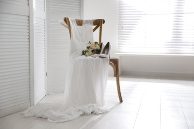 White high heel shoes, flowers and wedding dress on wooden chair indoors. Space for text
