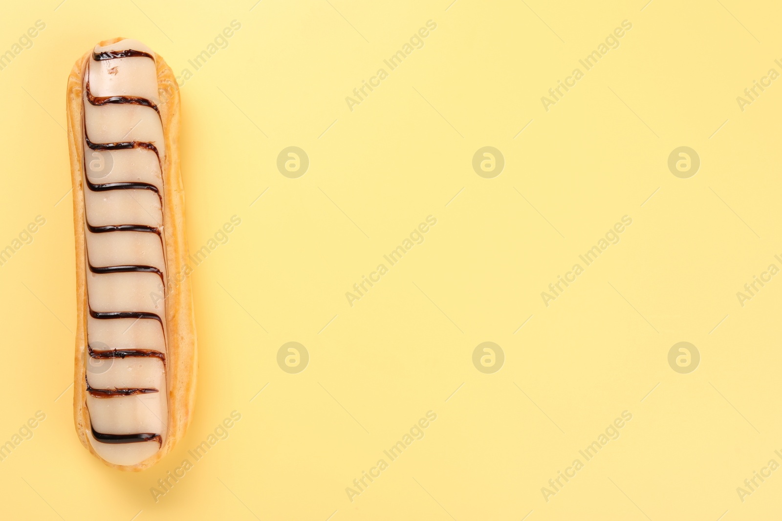 Photo of Delicious eclair covered with glaze on yellow background, top view. Space for text