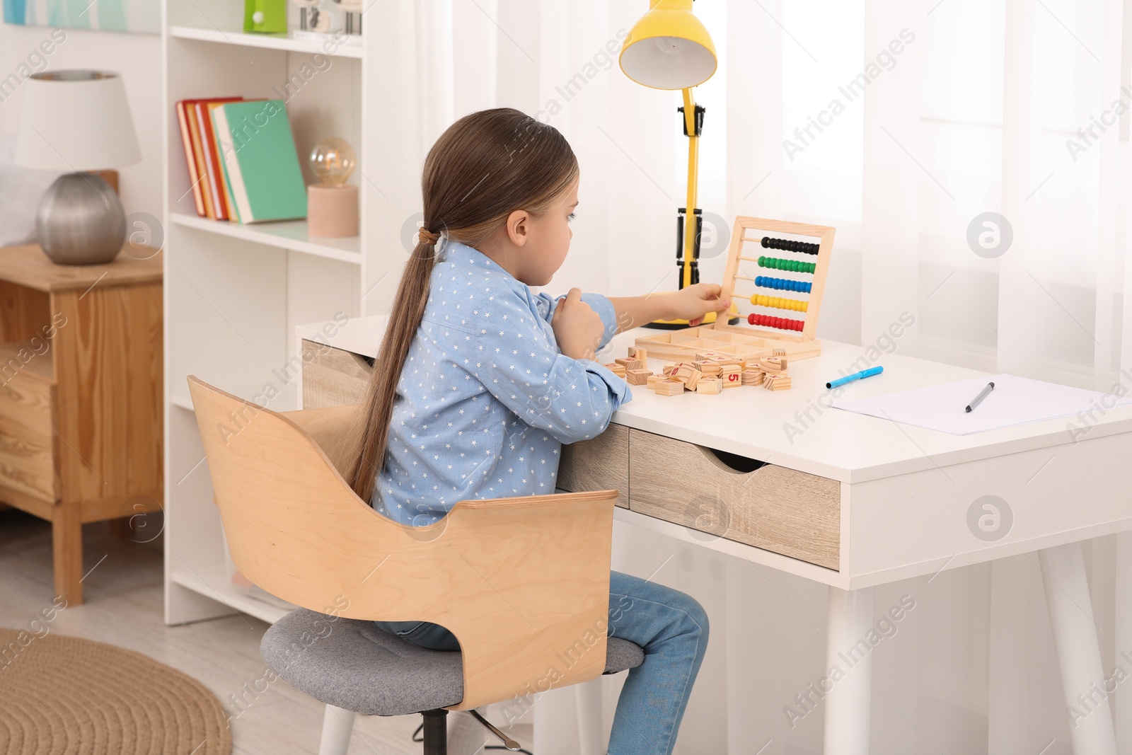 Photo of Girl with colorful abacus and wooden cubes at desk in room. Home workplace