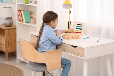 Girl with colorful abacus and wooden cubes at desk in room. Home workplace