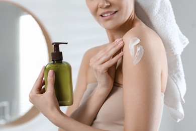 Photo of Woman applying body cream onto shoulder in bathroom, closeup