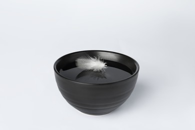 Water with feather in black bowl on white background