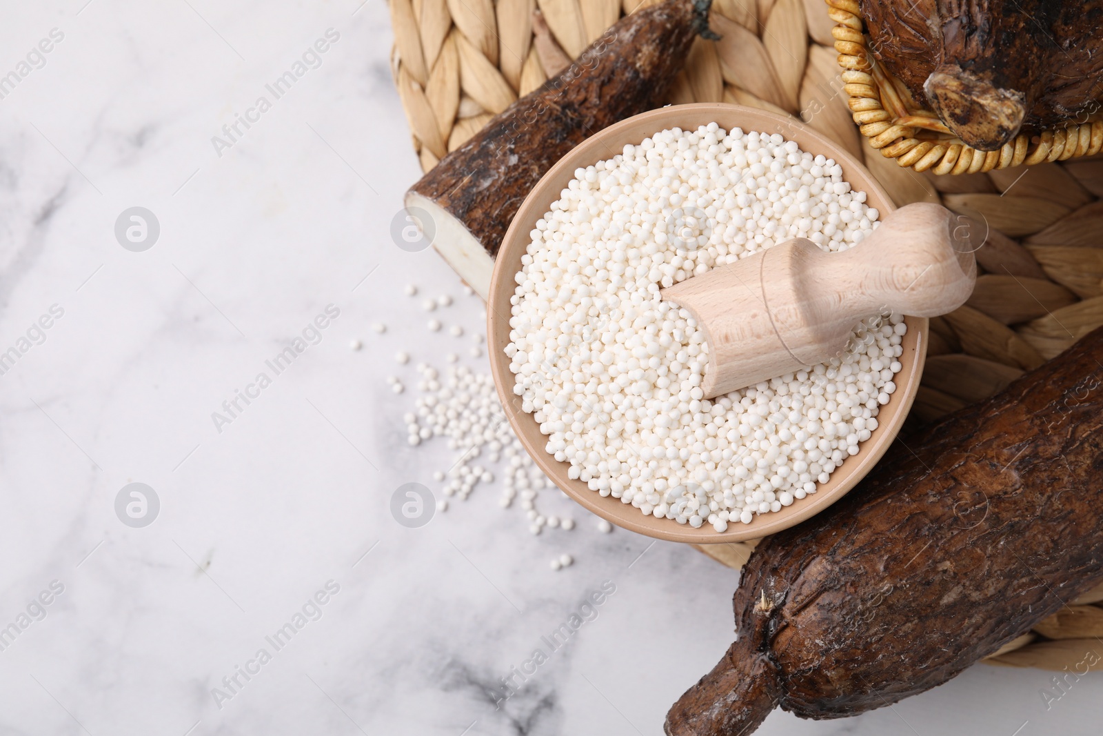 Photo of Tapioca pearls in bowl and cassava roots on white table, flat lay. Space for text