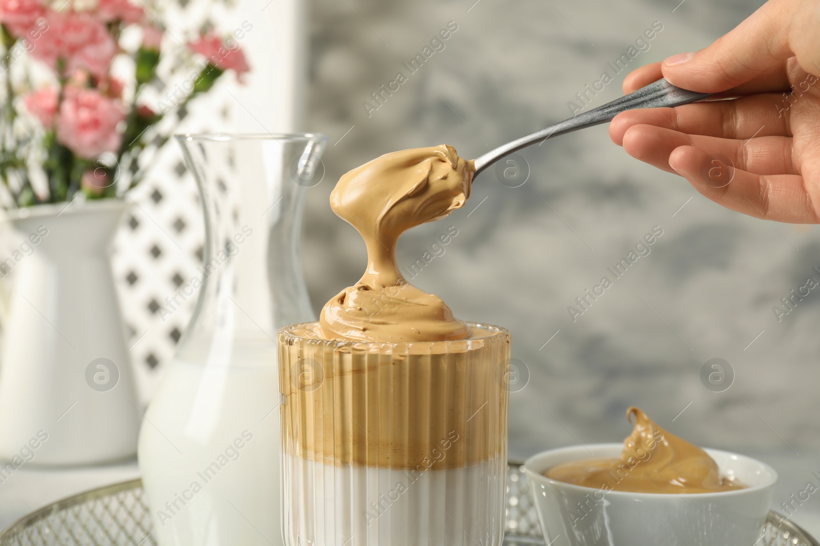 Photo of Woman pouring cream for dalgona coffee into glass indoors, closeup