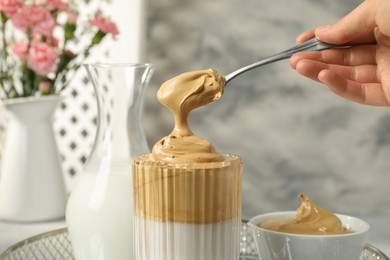 Woman pouring cream for dalgona coffee into glass indoors, closeup