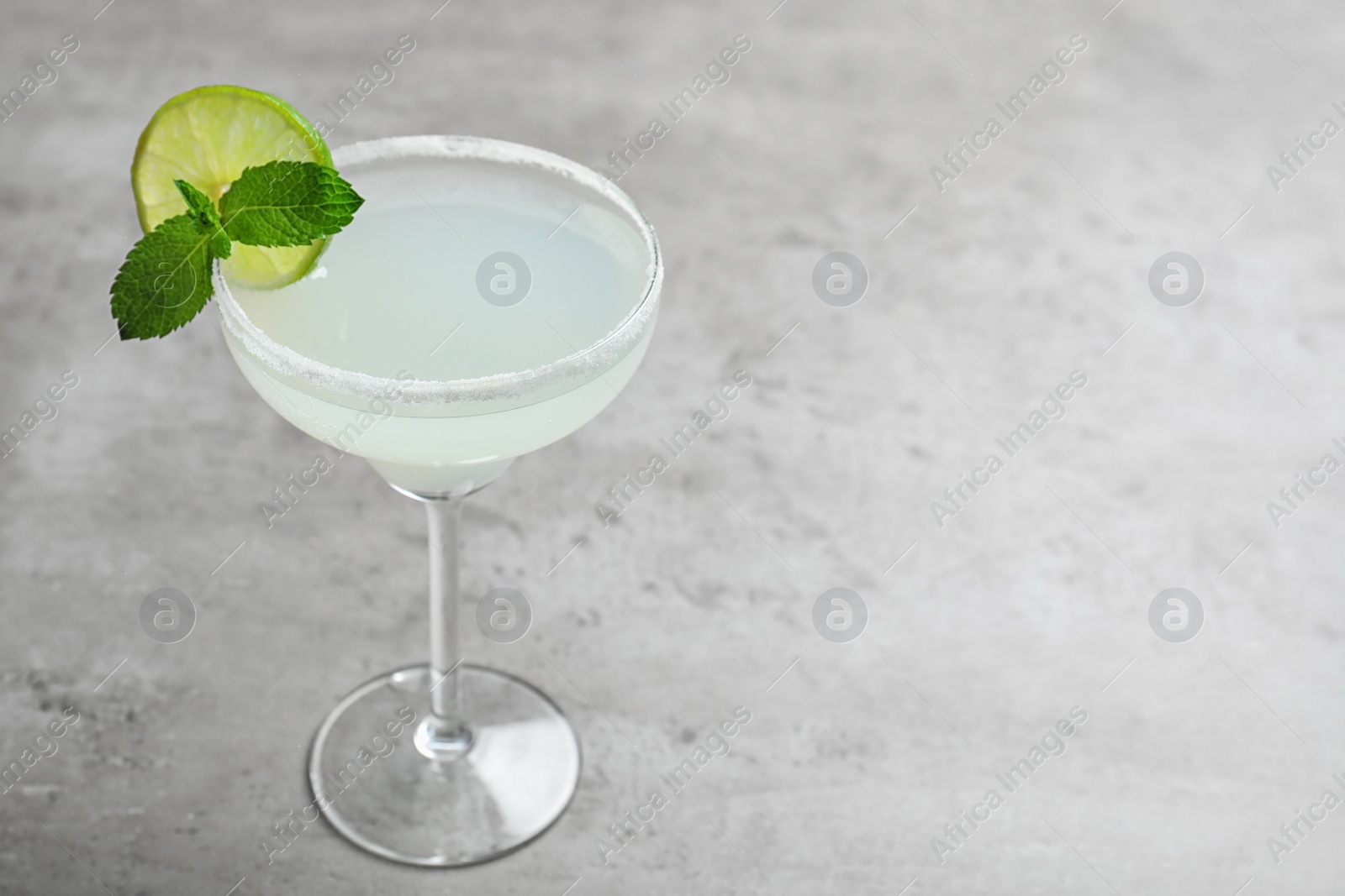 Photo of Glass of tasty refreshing cocktail with mint and lime on grey table. Space for text