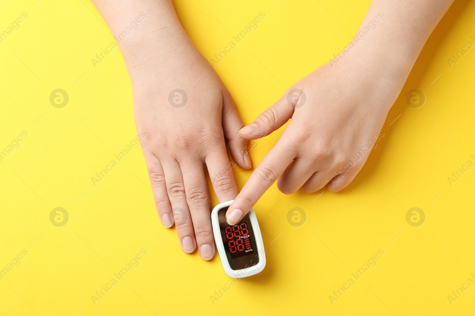 Photo of Woman using fingertip pulse oximeter on yellow background, top view