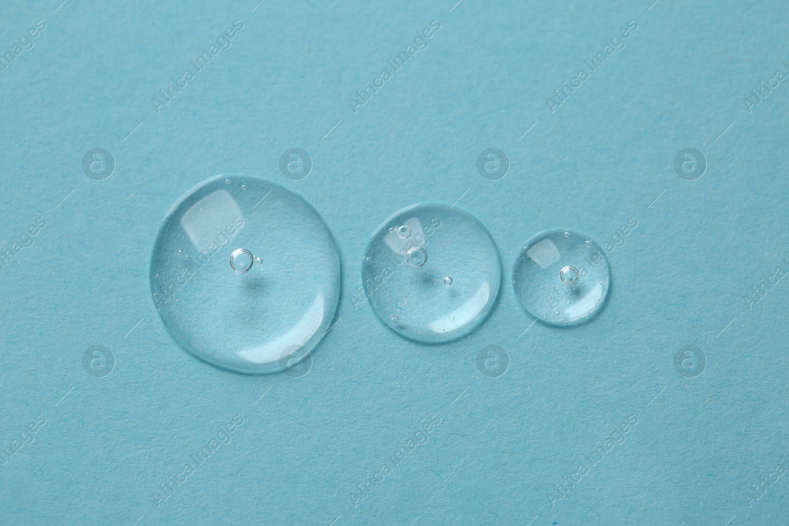 Photo of Drops of cosmetic serum on light blue background, top view
