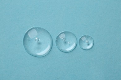 Drops of cosmetic serum on light blue background, top view