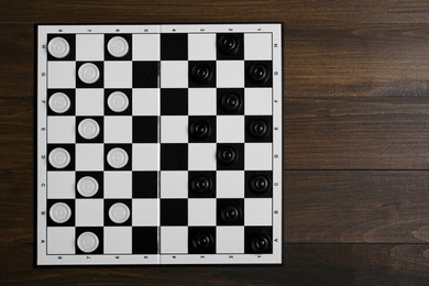 Photo of Checkerboard with game pieces on wooden table, top view. Space for text