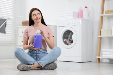 Photo of Woman sitting on floor and holding fabric softener in bathroom, space for text