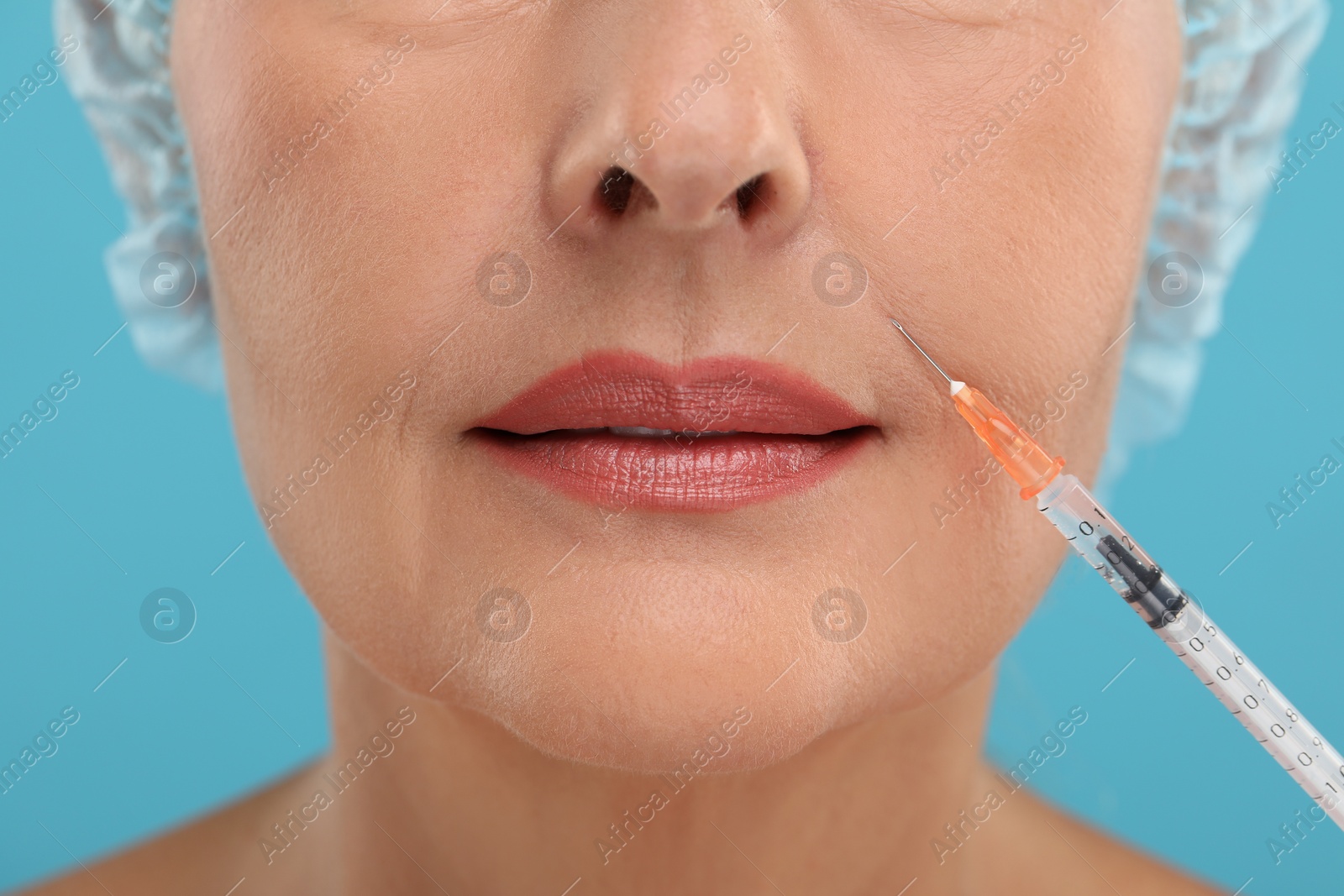 Photo of Senior woman getting facial injection on light blue background, closeup. Cosmetic surgery