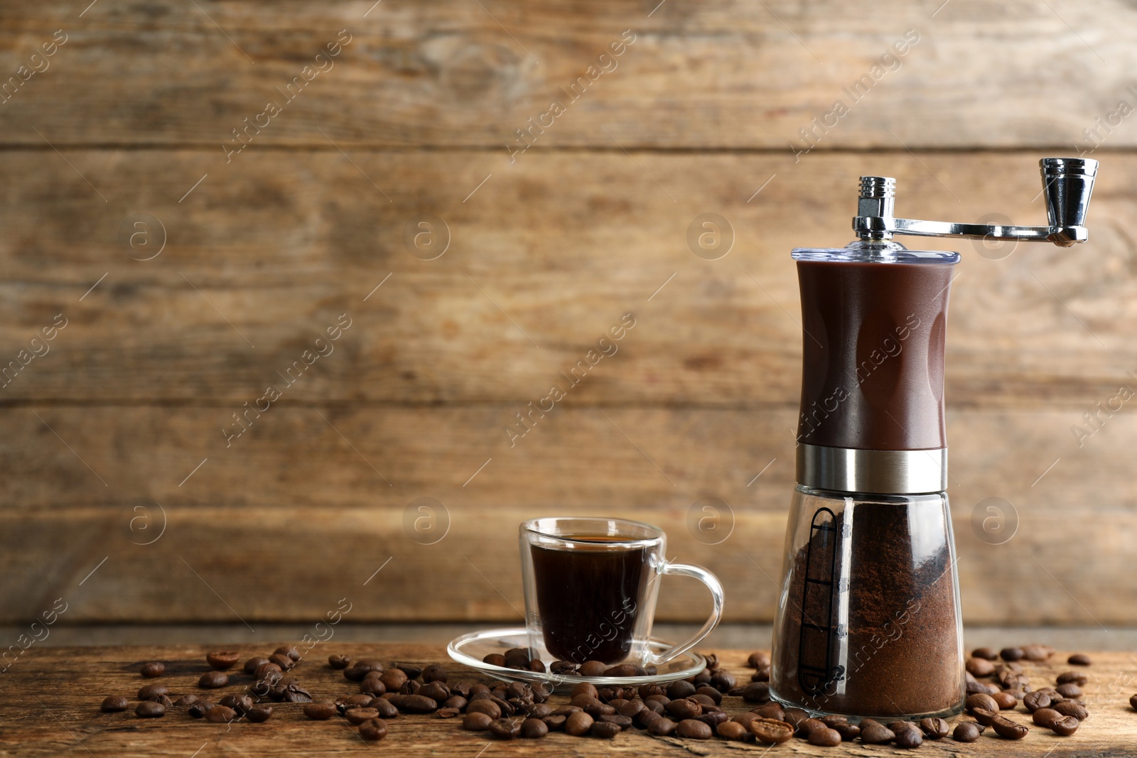 Photo of Manual coffee grinder with powder, beans and cup of drink on wooden table. Space for text