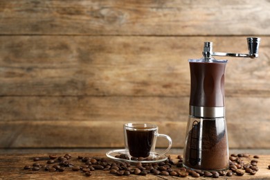 Manual coffee grinder with powder, beans and cup of drink on wooden table. Space for text