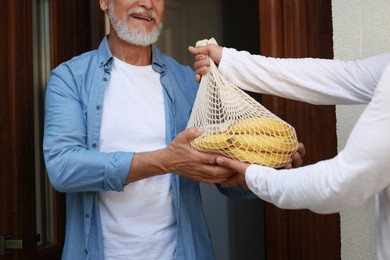Photo of Man with net bag of products helping his senior neighbour outdoors, closeup