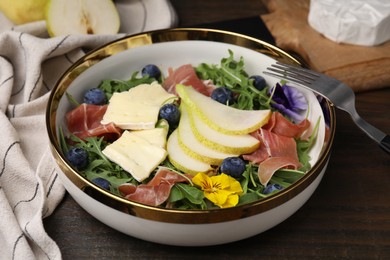 Photo of Tasty salad with brie cheese, prosciutto, blueberries and pear on wooden table