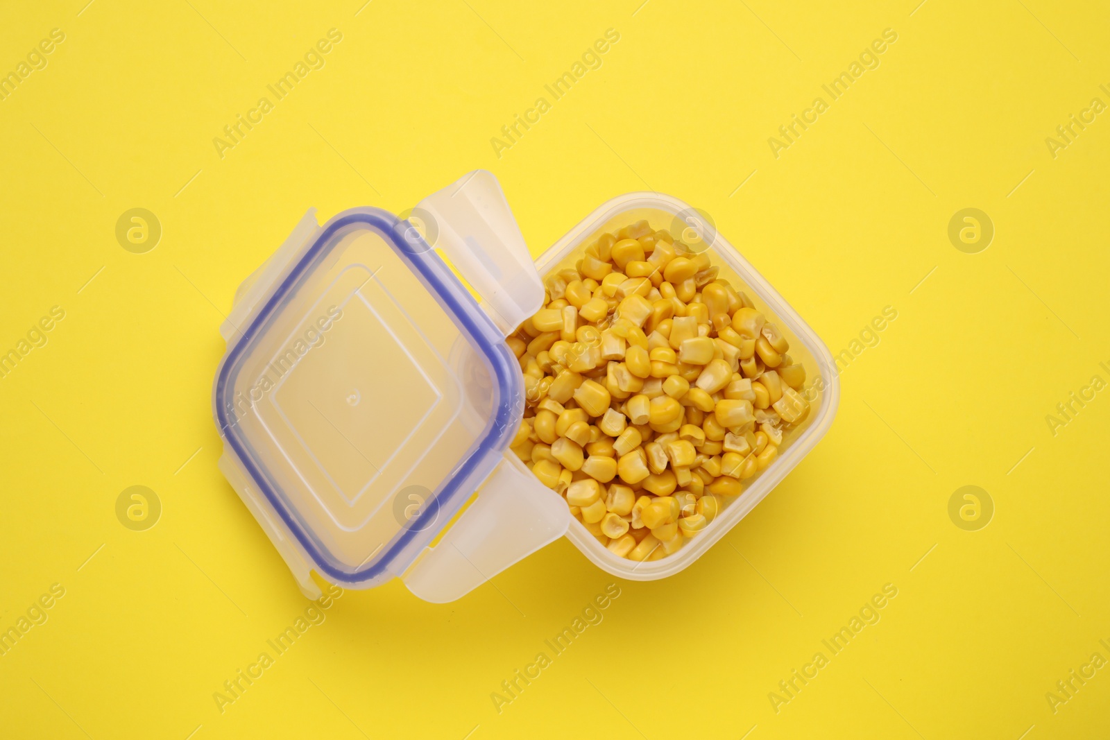 Photo of Plastic container with corn kernels and lid on yellow background, top view