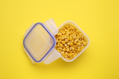 Photo of Plastic container with corn kernels and lid on yellow background, top view